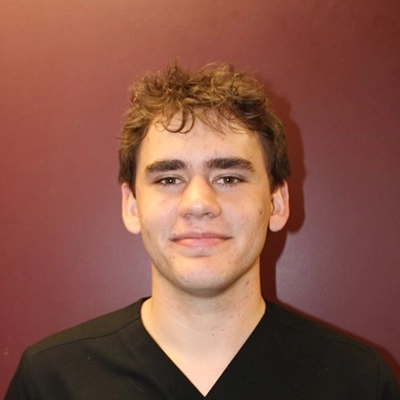 Brendan smiling in front of a maroon wall.